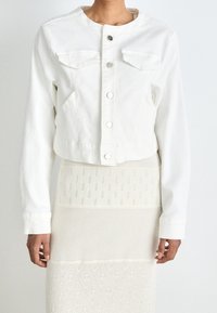 Valkoinen lyhyt farkkutakki, jossa on pitkät hihat, edessä napitus ja kaksi rintataskua. Sujuva pinta ja yksinkertainen muotoilu.