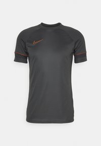 Tummanharmaa urheilupaita lyhyillä hihoilla, jossa on oransseja yksityiskohtia ja Nike-logo vasemmassa rinnassa. Silkkinen, kevyt kangas.