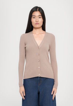 Cardigan beige a coste con scollo a V e maniche lunghe, con cinque bottoni sul davanti. Abbinato a jeans a gamba larga di un blu scuro.