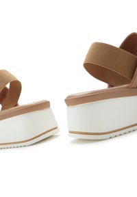 Brown platform sandals featuring elastic straps, a smooth upper, and a white wedge sole with a textured bottom for grip.