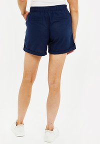 Pantalones cortos de lino azul marino con un corte relajado, cinturilla elástica, dobladillos enrollados y dos bolsillos traseros. Combinados con zapatillas blancas.