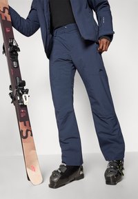 Marineblå skibukser med en lige pasform, vandtæt stof og forstærkede knæ. Har sidelommer og et logo ved taljen.