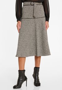Grauer und schwarzer Tweed-Midi-Rock mit hoher Taille, Gürtelschlaufen und A-Linie-Silhouette. Trägt schwarze Ankle Boots.
