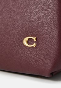 Burgundy leather handbag with a textured surface and a prominent gold 'C' logo accent. Smooth finish with a slightly structured shape.