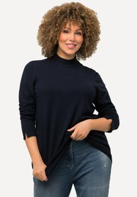 Mörkblå ribbad trikåtröja med hög hals, långa ärmar med tumhål och avslappnad passform. Bärs över urtvättade blå jeans.