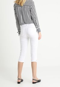 White cropped pants paired with a black and white striped button-up shirt. Black flats feature a dotted strap.
