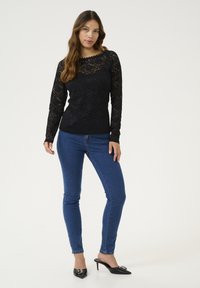 Must mustriga pikka varrukatega tees, millel on laineäär, kombineeritud sobivate siniste teksade ja kaunistustega mustade kontsakingadega.