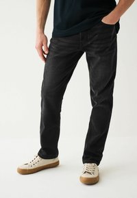 Blugi din denim negri cu un design drept, având o nuanță închisă, o textură subtilă și un stil clasic cu cinci buzunare. Asortați cu adidași deschiși.