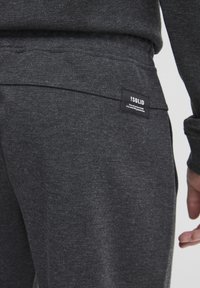 Gray textured fabric joggers with a back pocket featuring a black label reading "!SOLID" and additional text, medium-rise waist.