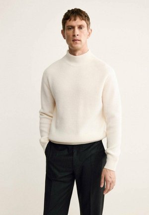 Maglione bianco a collo alto a coste con maniche lunghe, abbinato a pantaloni neri a righe sottili. Texture liscia e design aderente.