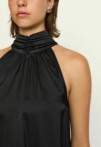 Top negru cu gât halter, realizat dintr-un material satinat neted, având detalii pliate la decolteu și un design elegant, fără mâneci.