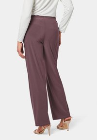 Wijduitlopende broek in een diepe mauve kleur, gemaakt van gladde stof. Heeft een elastische tailleband en een vloeiende silhoeet. Gecombineerd met beige hakken.