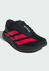 Scarpa sportiva nera con tomaia testurizzata, caratterizzata da audaci strisce rosse e un design aderente. Suola spessa per ammortizzazione e supporto.