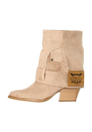 Beige ruskind mid-kalv støvle med stablet træhæl, spids tå, remdetalje og brun læderlap med sort grafik på ydersiden.