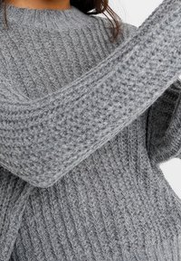 Gray knitted sweater with ribbed texture and wide sleeves, featuring a round neckline and a soft, chunky appearance.