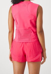 Top deportivo rosa con un bolsillo de malla en la parte trasera, combinado con pantalones cortos texturizados a juego. La tela parece ligera y transpirable.