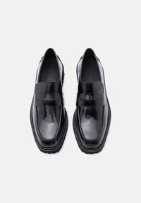 Fekete bőr lakkcipők, fényes befejezéssel, gumitalppal és jellegzetes elülső pánt részlettel. Lekerekített orr és minimális varrási díszítések.