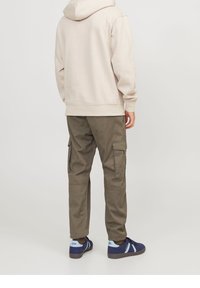 Ljust beige hoodie med avslappnad passform, tillsammans med olivgröna cargobyxor med sidofickor. Blå och marinblå sneakers fulländar looken.