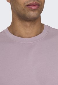 Camiseta de cuello redondo en color lila, confeccionada en suave algodón. Presenta un corte clásico con un cuello acanalado y una textura lisa.