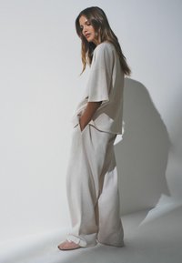 Beige übergroßes T-Shirt und passende weite Hose aus weichem Stoff. Merkmale: entspannte Passform und tiefe Seitentaschen; weiche rosa Schuhe.