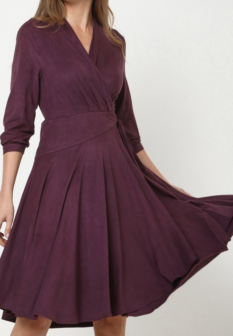 Lila Wickelkleid mit dreiviertelärmel, tailliertem Schnitt und gefaltetem Rock. Hergestellt aus weichem Stoff mit sanfter Textur.