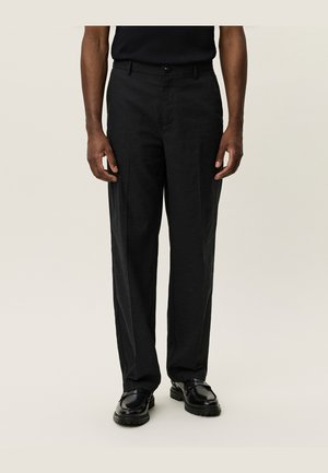 Pantalons noir ajustés avec une coupe droite, en tissu lisse. Comprend une fermeture à bouton et des passants de ceinture, assortis à des chaussures noires.