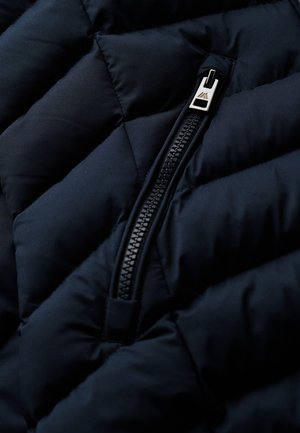 Marine-blauwe gewatteerde jasstof met een close-up weergave van een zijrits, voorzien van een slanke zilveren trekker en een gestructureerd patroon van padding.
