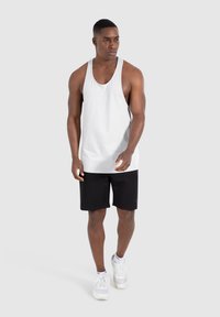 Lichtgrijze mouwloze tanktop gecombineerd met zwarte shorts, met een relaxte pasvorm en zachte stof. Witte sneakers complementeren de outfit.