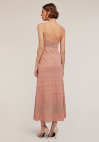 Takakatsomwa ya vestido maxi ya pink, isiyo na mikono, yenye muundo wa maandiko ya kuvutia, mwili ulio karibu na mwili, na sketi inayotiririka, pamoja na viatu vya kisasa vyenye visigino.