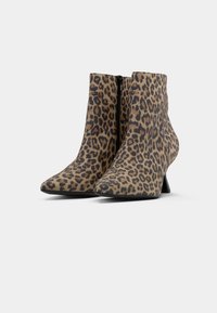 Un paio di stivali a punta con altezza alla caviglia, con stampa leopardata e zip laterale nera, posizionati su uno sfondo grigio chiaro uniforme.