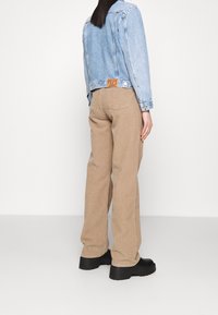 Ljusblå denimjacka med en kortad design, tillsammans med gräddfärgade kordbyxor med hög midja och svarta platåskor, sett från ryggen.