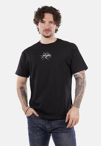 T-shirt nera in cotone con colletto rotondo e maniche corte, caratterizzata da una stampa grafica bianca sulla parte anteriore. Vestibilità comoda, texture liscia.