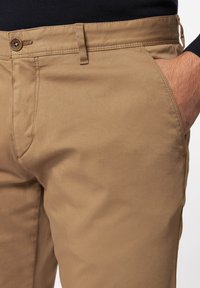 Tan katoenen chino's met een gladde textuur, een platte voorkant, zijzakken en een enkele knoopsluiting bij de taille. Gedetailleerde stiknaden zichtbaar.
