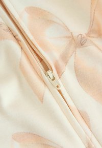 Gaismas audums ar persiku un krēmkolorainu ziedu rakstu, ar krēma krāsas rāvējslēdzēju. Mīksta tekstūra ar redzamām šuvju detaļām.