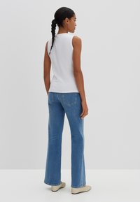 Top bianco senza maniche in tessuto texturizzato, abbinato a jeans svasati di colore blu chiaro. Footwear beige, con un design semplice.