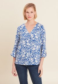 Blusa a fiori blu e bianchi con scollatura a V, maniche a tre quarti e vestibilità ampia, realizzata in tessuto leggero. Abbinata a jeans in denim scuro.