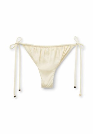 Bas de bikini couleur crème avec des liens de chaque côté, présentant un design froncé et une couverture minimale. Texture douce et lisse avec des accents en métal carré.
