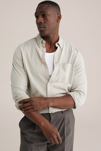 Šviesiai smėlio spalvos marškiniai su sagomis, krūtinės kišene, rankovėmis susuktais į viršų, derinami su tamsiomis languotomis kelnėmis. Audinys su tekstūra, neutralios spalvos.