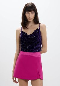 Top in paillettes viola con spalline sottili abbinato a una mini gonna rosa brillante con uno spacco laterale; enfasi sulla texture e sul contrasto di colori.
