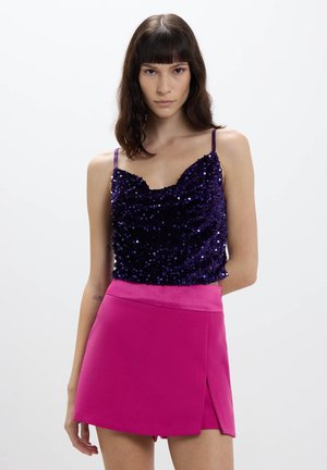 Top in paillettes viola con spalline sottili abbinato a una mini gonna rosa brillante con uno spacco laterale; enfasi sulla texture e sul contrasto di colori.