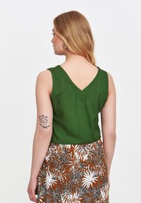 Zielony top bez rękawów z dekoltem w kształcie litery V i gładką teksturą, połączony z brązową spódnicą w kwiatowy wzór z białymi akcentami.