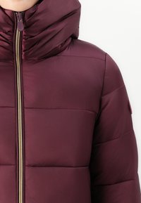 Bordeaux puffer jack met een hoge kraag, voorzien van een gouden rits en een gewatteerde textuur. Inclusief een logo accent op de mouw.