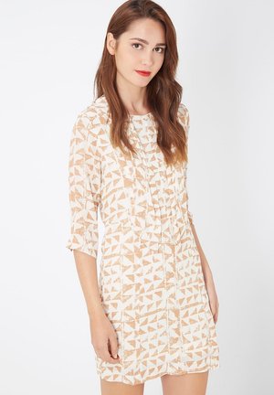 Vestido de manga corta en crema con un patrón geométrico en beige. Presenta un corte holgado y una tela ligera y texturizada.