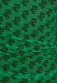 Tissu vert avec des motifs abstraits noirs répétés, présentant une surface texturée et un design froncé.