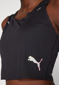 Čierny športový crop top s textúrovanou, priedušnou tkaninou. Reflexné akcenty a logo s poskakujúcim mačkovitým predátorom v bielej a žltej farbe na prednej strane.