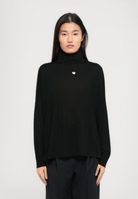 Čierny rolák vyrobený z mäkkej tkaniny, s malým bielym srdiečkom na hrudníku a voľným, oversized strihom.