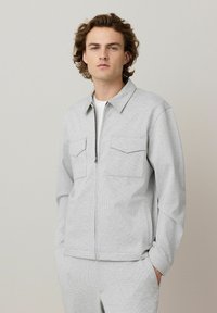 Lys grå zip-up jakke lavet af tekstureret stof, med krave, to brystlommer og en generelt afslappet pasform.