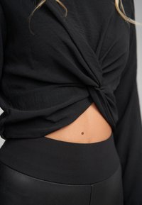 Czarna bluzka z długim rękawem z przednim skręceniem, odsłaniająca skórę. Dopasowana do legginsów z wysokim stanem w kolorze czarnym, z gładkim pasem.