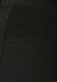 Černá elastická tkanina ukazující detailní pohled na hladkou strukturu, s viditelnými švy podél švu a oblasti kapsy.