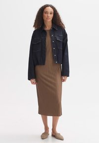 Dunkelblaue, cropped Jeansjacke mit zwei Brusttaschen, kombiniert mit einem braunen, gerippten Midikleid und beigen Slippers. Glatte Textur, einfaches Design.